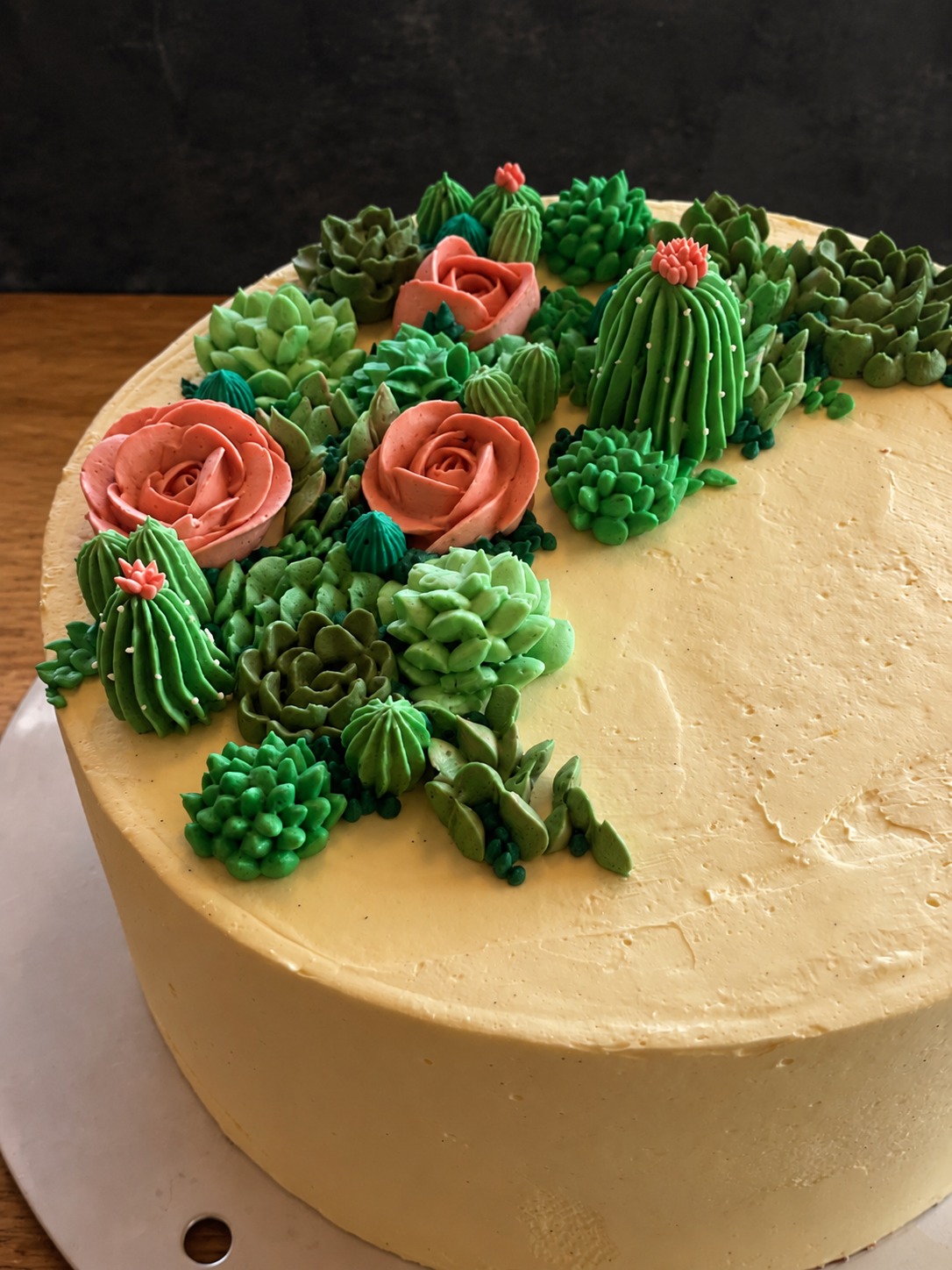Torte mit grünen Sukkulenten und rosa Blüten aus Creme